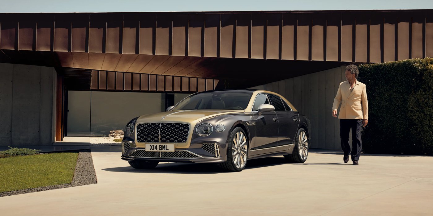 Bentley Glasgow Bentley New Flying Spur Mulliner V8 hybrid sedan front three quarters in Rose Gold over Magnetic paint, parked near modern home