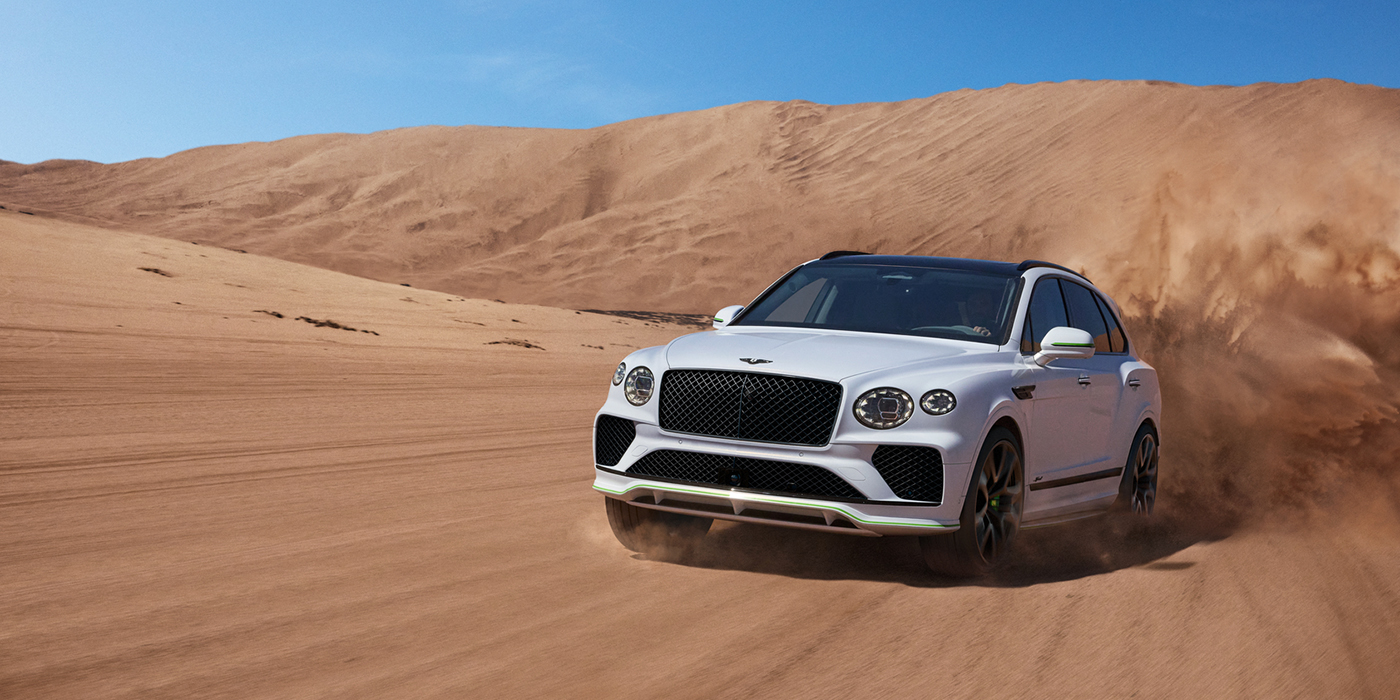 Bentley Glasgow Bentley Bentayga Speed SUV front three quarter in Snow Quarts Pearlescent by Mulliner white paint driving dynamically through the desert