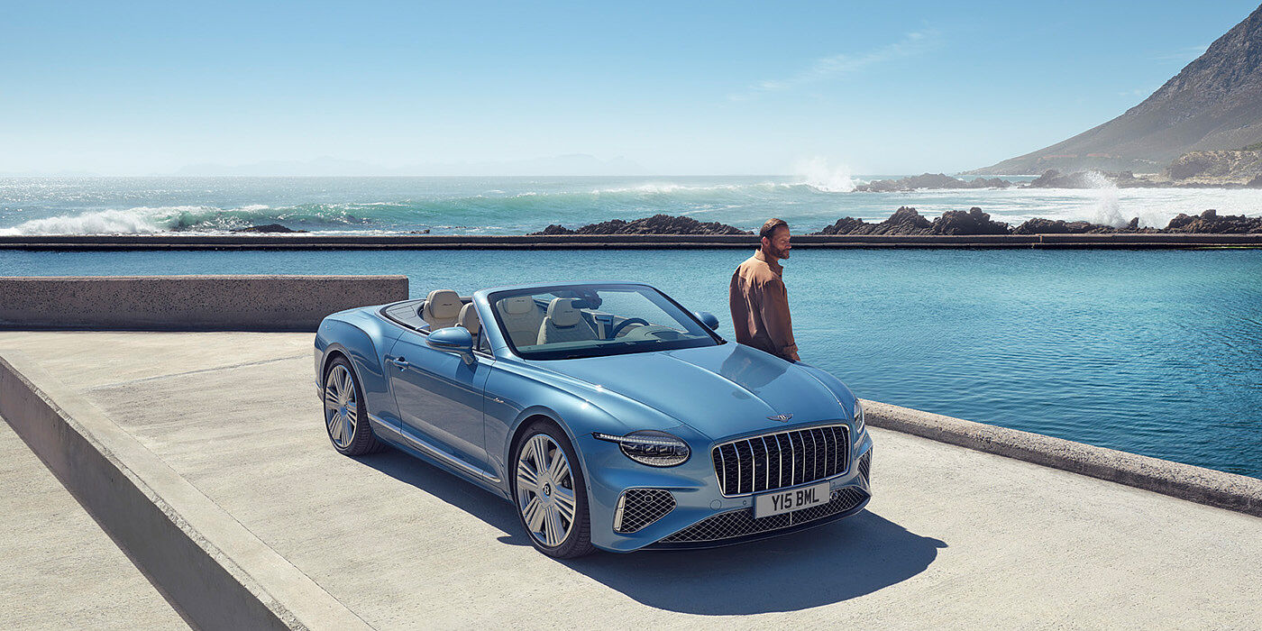 Bentley Glasgow New Bentley Continental GTC Azure convertible front view in Light Windsor blue paint with 22 inch ten spoke wheels parked by the sea in the sunshine