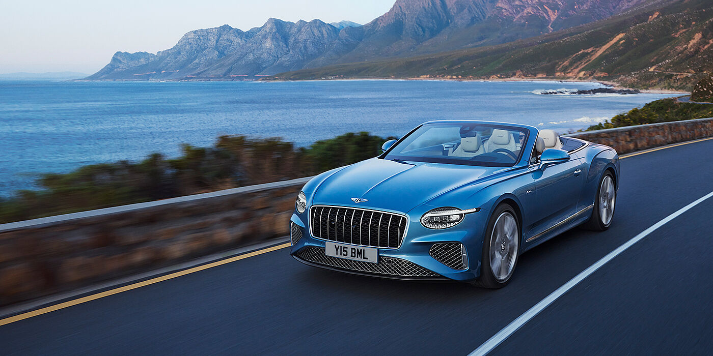 Bentley Glasgow New Bentley Continental GTC Azure convertible in Light Windsor blue paint with 22 inch Azure wheels and chrome grill, driving dynamically by the sea