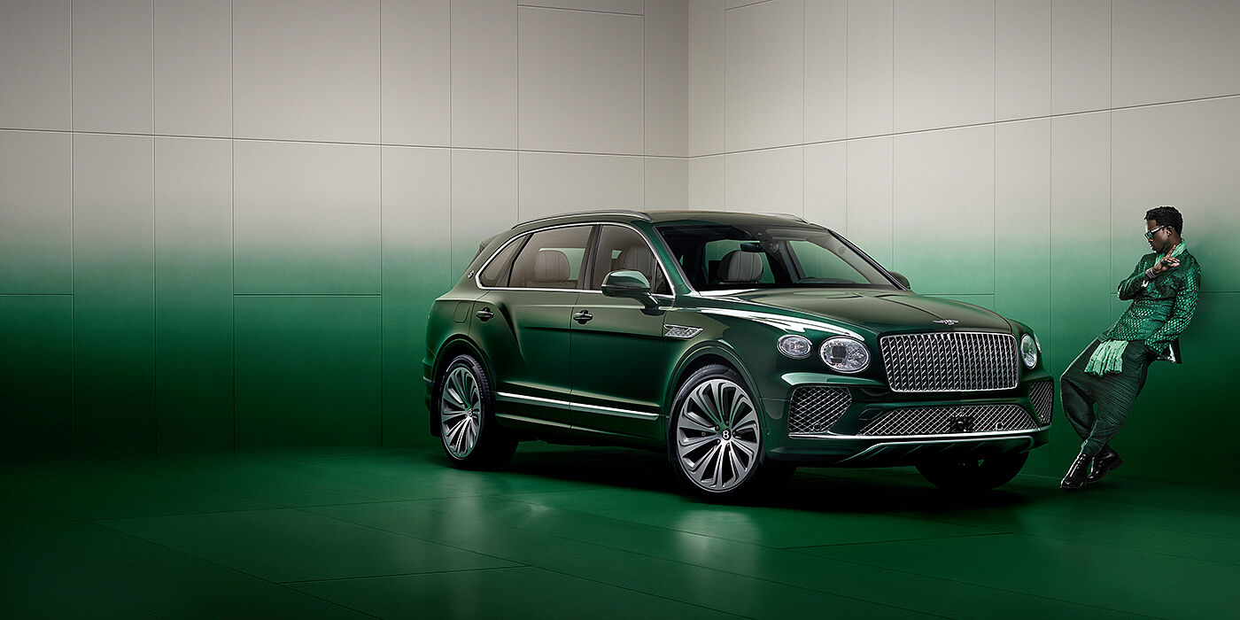 Bentley Glasgow Wisdom K leans against wall next to Bentley Bentayga Extended Wheelbase Atelier Edition SUV in Light Emerald green paint