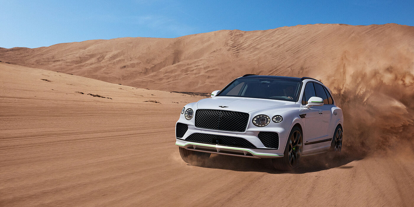 Bentley Glasgow Bentley Bentayga Speed SUV front three quarter in Snow Quarts Pearlescent by Mulliner white paint driving dynamically through the desert