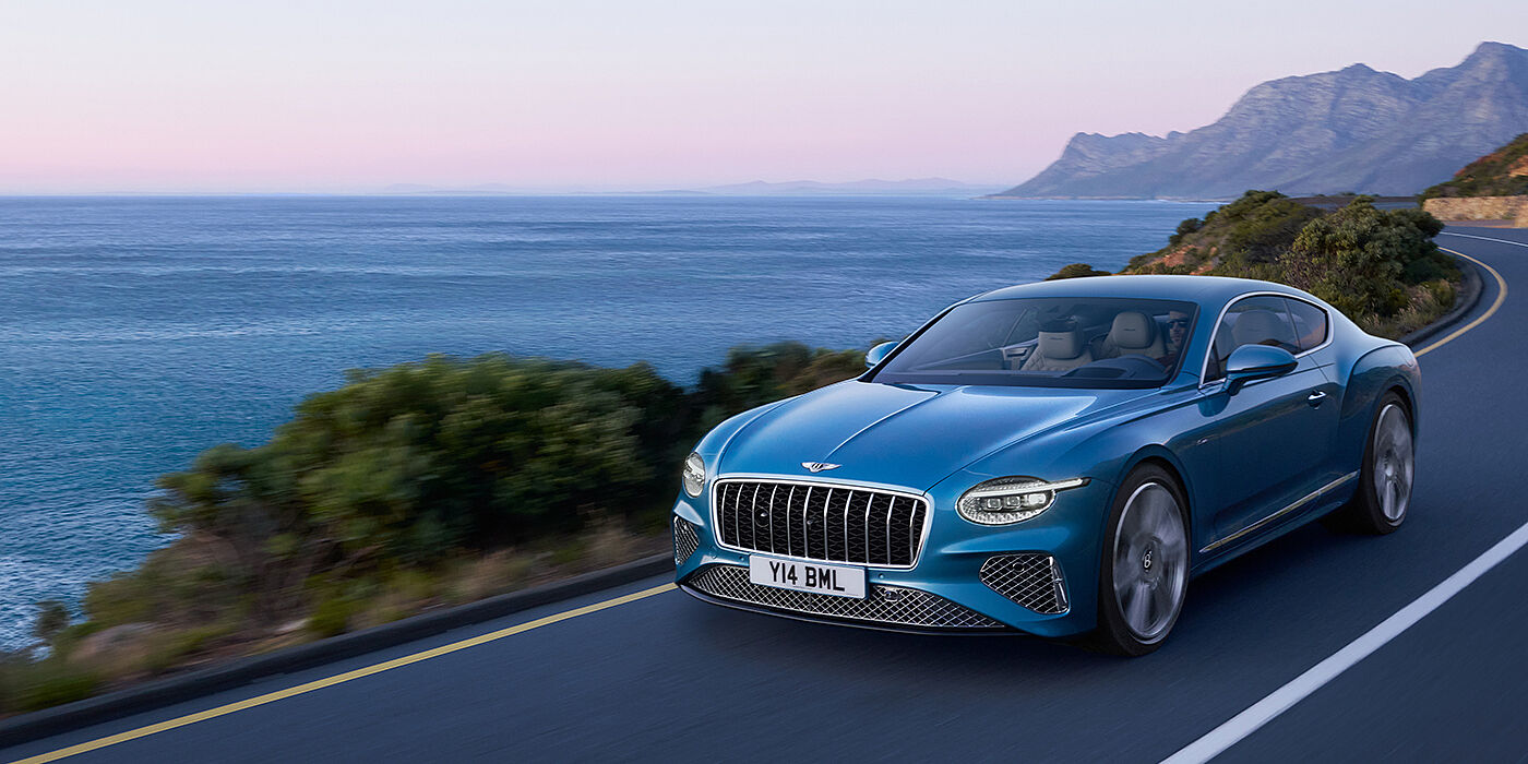 Bentley Glasgow New Bentley Continental GT Azure coupe in Light Windsor blue paint with 22 inch Azure wheels and chrome grill, driving dynamically by the sea