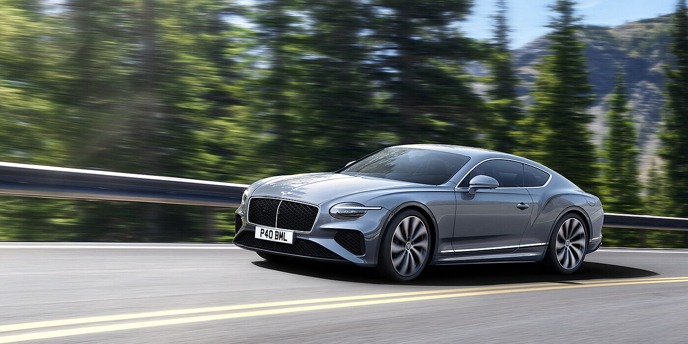 Bentley Glasgow New Bentley Continental GT coupe in Silverlake paint and 22 inch ten-spoke wheels, driving dynamically on a tree-lined road in the sunshine