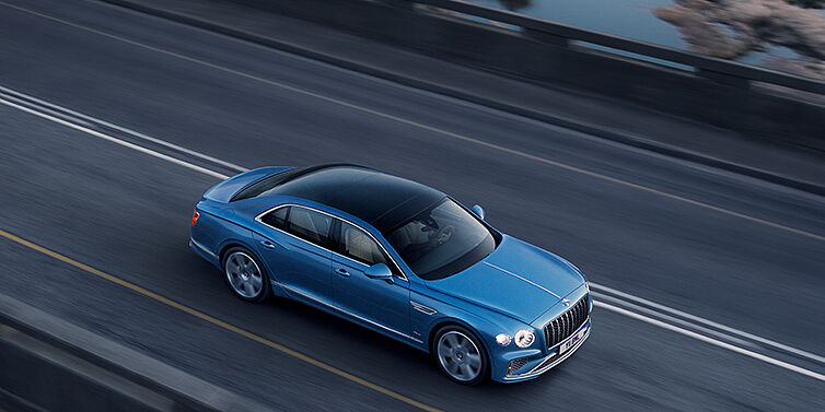 Bentley Glasgow New Bentley Flying Spur Azure sedan in Light windsor blue paint by Mulliner, with 22 inch Azure wheels seen from overhead driving dynamically on a country road