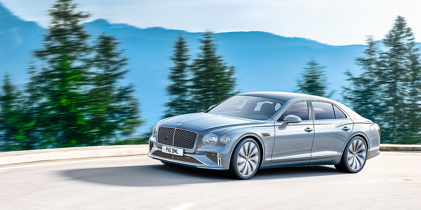 Bentley Glasgow New Bentley Flying Spur sedan side view in Silverlake paint with ten spoke wheels and chrome matrix grille driving dynamically on a mountain road