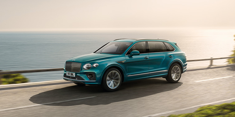 Bentley Glasgow Bentley Bentayga Extended Wheelbase Azure SUV in Topaz blue paint driving dynamically by the ocean