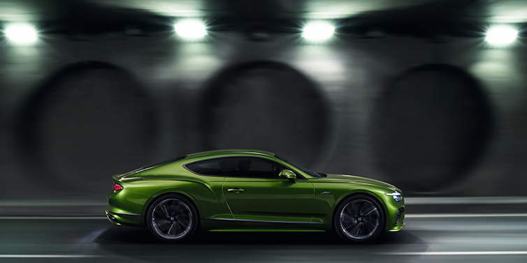 Bentley Glasgow Bentley Continental GT Speed coupe profile in Tourmaline Green driving dynamically past a concrete wall at night