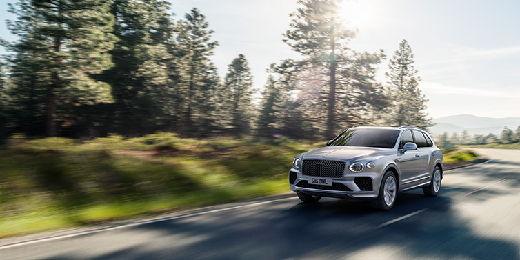 Bentley Glasgow Bentley Bentayga SUV front three quarter in Moonbeam silver paint driving dynamically along a tree-lined road