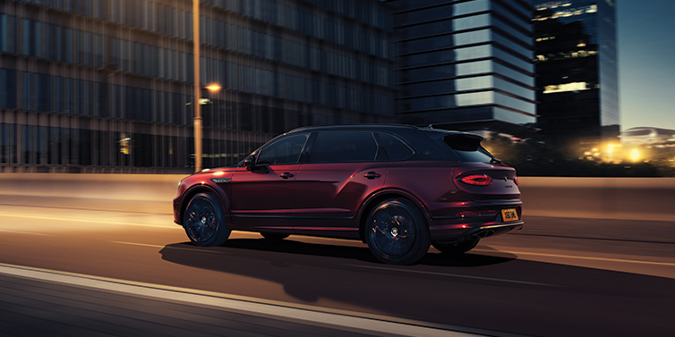 Bentley Glasgow Bentley Bentayga Extended Wheelbase Mulliner SUV in Cricket Ball red paint driving dynamically in city at night