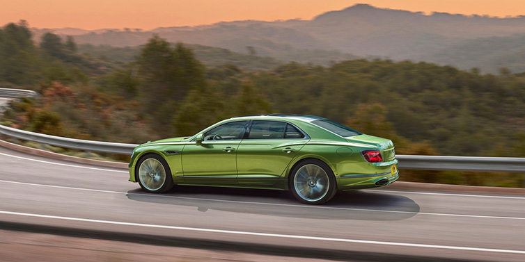 Bentley Glasgow Bentley Flying Spur Speed sedan side profile in Tourmaline Green paint driving dynamically on a mountain road at sunset