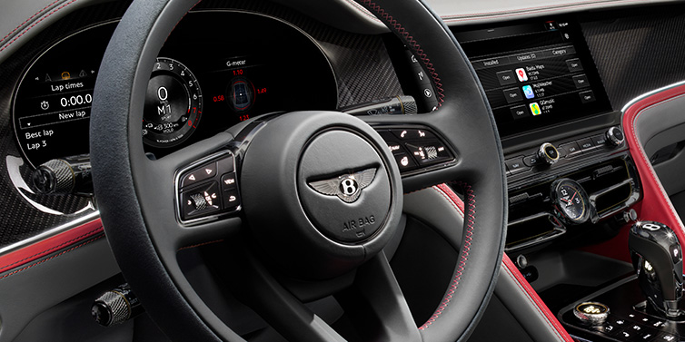 Bentley Glasgow Bentley Flying Spur Speed sedan front interior detail showing steering wheel and driver screens surrounded with Hotspur red and Gravity Grey hides